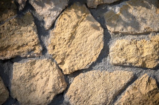 The sunlight casts gentle shadows on a rustic stone wall, revealing its unique textures and warm colors beautifully.