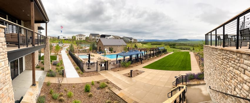 Castle Rock, Colorado, USA-June 11, 2023-A beautifully designed outdoor community pool surrounded by lounge chairs, umbrellas, and landscaped greenery. The fenced pool area includes shaded seating and a modern clubhouse in the background, creating a welcoming environment for relaxation and leisure.