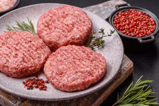 Fresh raw ground beef burger patty with salt and spices on textured concrete background