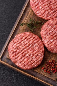 Fresh raw ground beef burger patty with salt and spices on textured concrete background