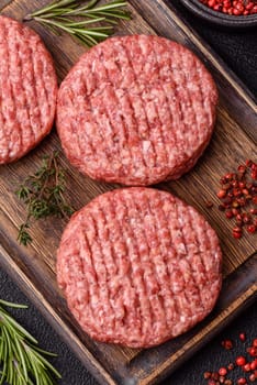 Fresh raw ground beef burger patty with salt and spices on textured concrete background