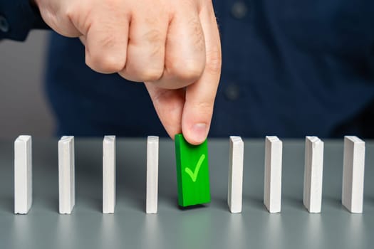 A man holds a green domino with a check mark. Checkpoint reached, milestone. Successfully completed. Ready for launch. Checking and verification. Start a business. A life stage that has been passed.