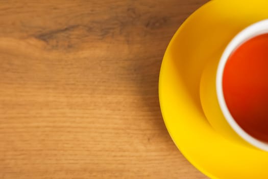 A yellow cup and saucer stands on a wooden background with black tea poured, half of a mug with space for text is visible. The concept of tea drinking, tea tradition, break. High quality photo