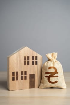 Wooden house figure and ukrainian hryvnia money bag. Taxes. Property value appraisal. Make a deal. Buying and selling real estate. Property Insurance. Housing prices.