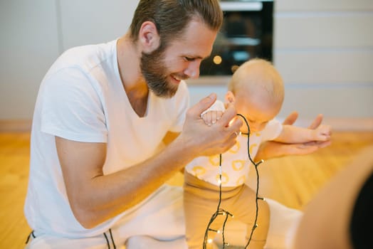 A loving father and his baby enjoy joyful moments surrounded by festive lights in a cozy, warm setting