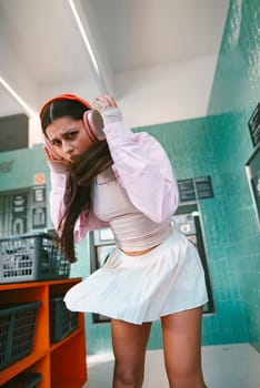 A fashionable and stylish woman happily enjoys listening to music while posing in a contemporary laundromat