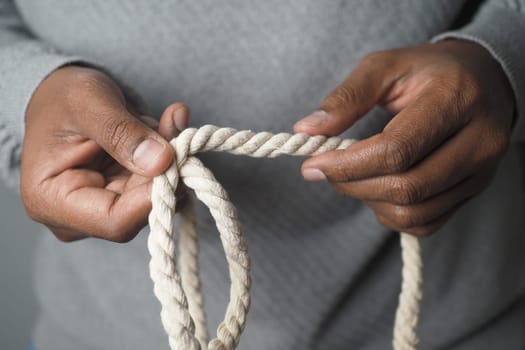 Hands carefully handling a thick rope, showcasing a crafting activity focused on creating knots or other designs. The setting is indoors with neutral lighting.
