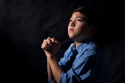 A young boy folds his hands and raises his head in prayer to God.