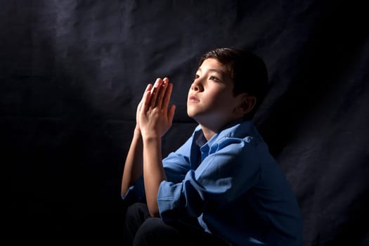 A young boy folds his hands and raises his head in prayer to God.