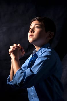 A young boy folds his hands and raises his head in prayer to God.