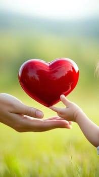 Child and adult hands holding a shiny red heart outdoors