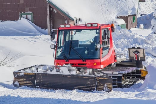 Snowy red groomer parking next to ski slope in mountain resort. Horizontally.  All potential trademarks are removed.