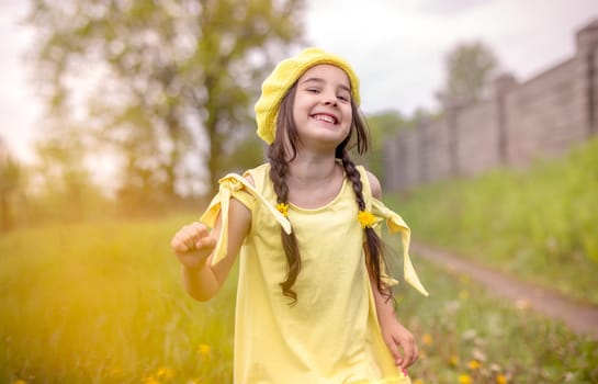 Cheerful and happy charming girl 4 years old in a yellow knitted beret and a yellow dress, dancing in nature in the spring, movement.