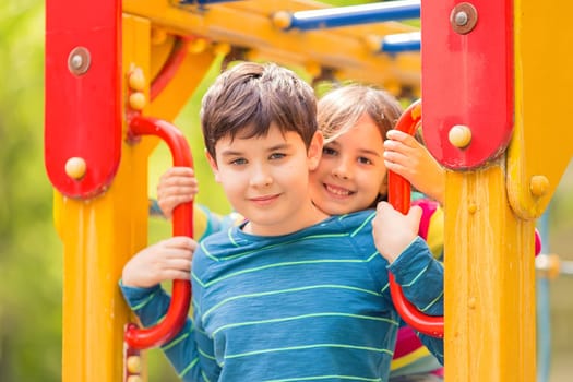 Smiling cute boy and girl, brunettes, stand among the yellow colorful playground, in the summer in the park, look at the camera. Close up