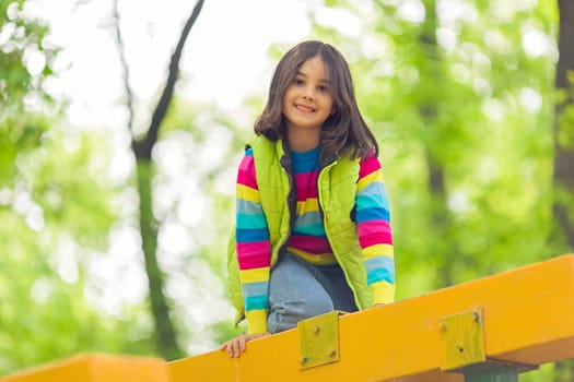 Portrait of a cute smiling little girl on a bright wooden platform in the park in spring