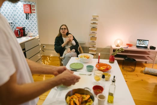 A warm and inviting family kitchen scene depicts a loving caregiver gently holding a baby while preparing food