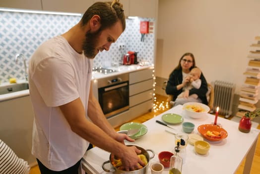 A cozy and warm kitchen scene featuring a man expertly preparing delicious food while a woman lovingly holds a baby