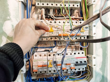 Kirov, Russia - November 26, 2024: Hand is seen working on an electrical switchboard, adjusting wires for proper function and ensuring safety in the system.