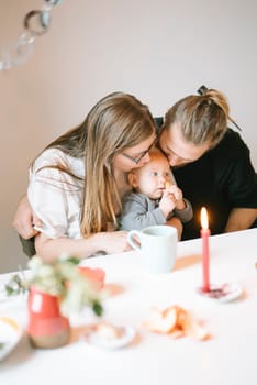 A loving family scene shows parents joyfully sharing a moment with their baby at a cozy table setting