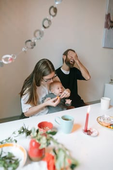 A joyful family moment as parents lovingly feed their baby, surrounded by warmth and laughter in the room