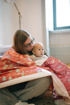 A serene moment with a parent and baby wrapped in a festive blanket, radiating warmth and connection.
