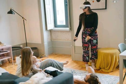In a bright and cozy living room, a woman fully enjoys her virtual reality experience while children watch her in awe