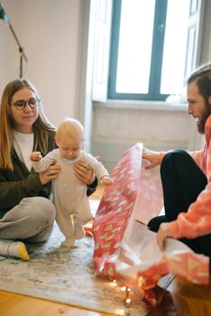 A wonderfully joyful family moment where a baby and adults are happily wrapping gifts together in a cozy setting