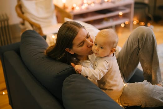 A loving mother tenderly kisses her adorable baby while sitting on a cozy couch, enveloped by warm, soothing lights