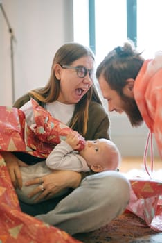 A family shares joy as they unwrap gifts with their baby, reflecting excitement in a delightful moment together