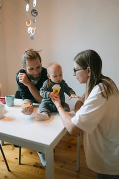 A warm, cozy family moment where parents joyfully share a delightful snack with their adorable baby at the dining table