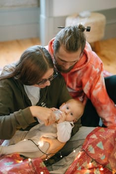 A loving family joyfully interacts with their adorable baby amidst beautifully warm decor and festive holiday lights