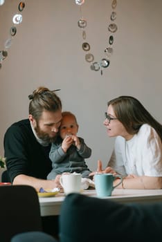 A loving couple joyfully shares a beautiful moment with their adorable baby in a cozy, warm cafe ambiance