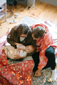 A heartwarming scene of two caring adults interact lovingly with a baby while sitting on a cozy, soft rug
