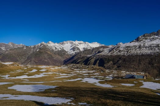 Snow rests on the ground beneath towering mountains, creating a peaceful winter landscape. Bright blue skies enhance the tranquility of this remote location.