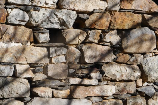 Weathered stones form a sturdy wall, each rock unique in shape and color. The sunlight casts shadows, highlighting the textures. This structure blends harmoniously with the environment.