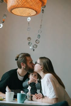 In a warm and cozy setting, a loving couple joyfully shares a tender kiss while lovingly holding their baby