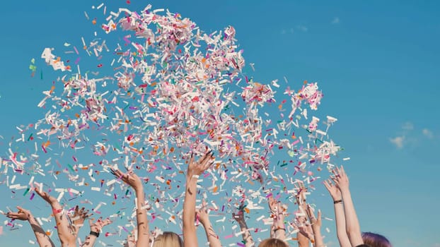 High school graduates joyfully tossing colorful confetti into the air against a backdrop of clear blue skies