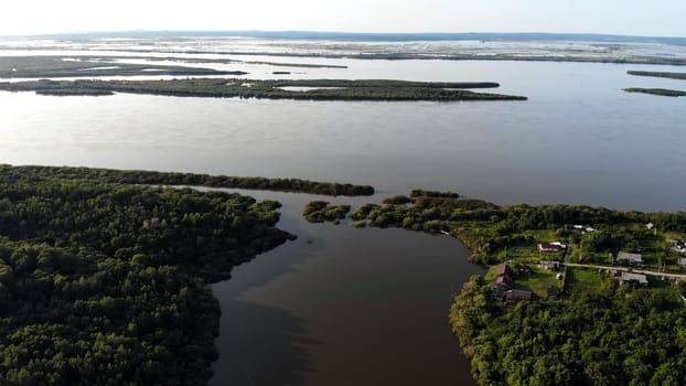 Breathtaking aerial view of a river confluence, showcasing lush green islands, tranquil waters, and a small cluster of houses nestled amidst nature