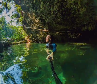 Man tourist in the water of a Mexican cenote surrounded by natural beauty. Adventure travel, eco-tourism, and exploration concept in a tropical paradise.