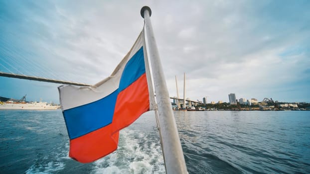 Russian national flag flying from vessel navigating eastern golden horn bay near zolotoy rog bridge in vladivostok waterfront