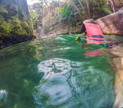 09.12.24, Playa Del Carmen, Mexico: Boy tourist in the water of a cenote at Xcaret park wearing a marked life jacket. Mexican tourism in natural parks. Adventure, childhood exploration, and eco-tourism concept in Quintana Roo.