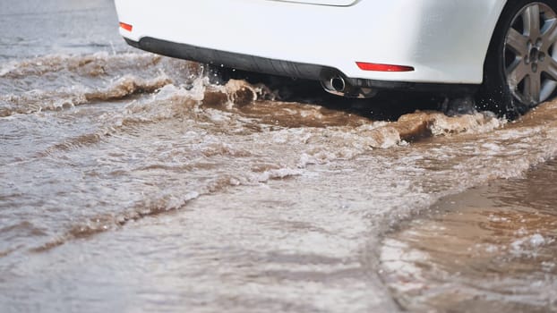 White car making waves driving through flooded street after heavy rain, creating a splash