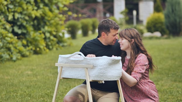 Loving parents gazing adoringly at sleeping newborn nestled peacefully in wooden crib under soft natural sunlight near garden setting