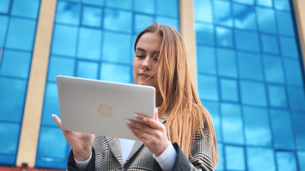 Young businesswoman using digital tablet in front of modern office building with blue glass facade