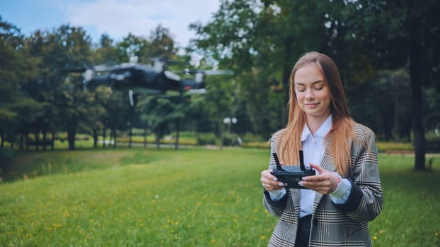 Professional female pilot controlling drone while walking through green park, demonstrating modern technological integration with nature
