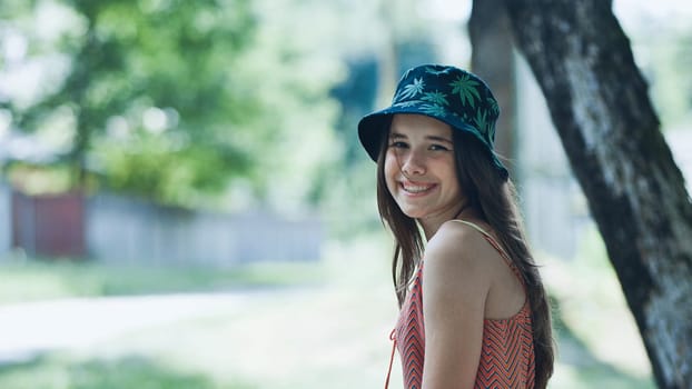 Portrait of a cheerful teenage girl wearing a bucket hat, enjoying a sunny summer day in a park