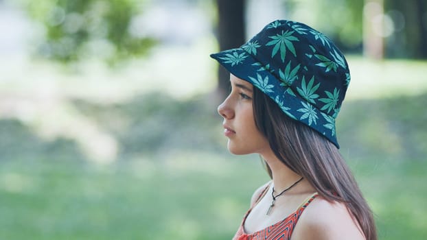 Teenage girl wearing a bucket hat with cannabis leaf prints, enjoying a summer day in a park