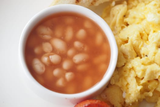 A delicious breakfast plate showcases fluffy scrambled eggs alongside a small bowl of baked beans, offering a hearty start to the day.