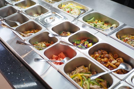 A buffet setup features neatly arranged trays filled with diverse dishes, including vegetables, proteins, and sauces. Diners can choose from a colorful assortment of food options.