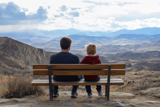 A father and son sit side by side on a wooden bench, gazing over a stunning mountain landscape under a dramatic sky.